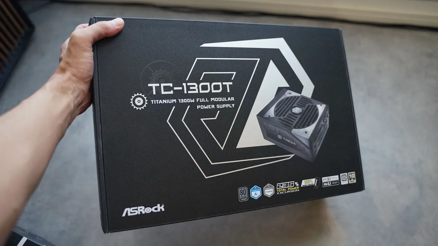 手に持ったASRock Taichi TC-1300Tのパッケージ。TITANIUM 1300W FULL MODULAR POWER SUPPLYの表記